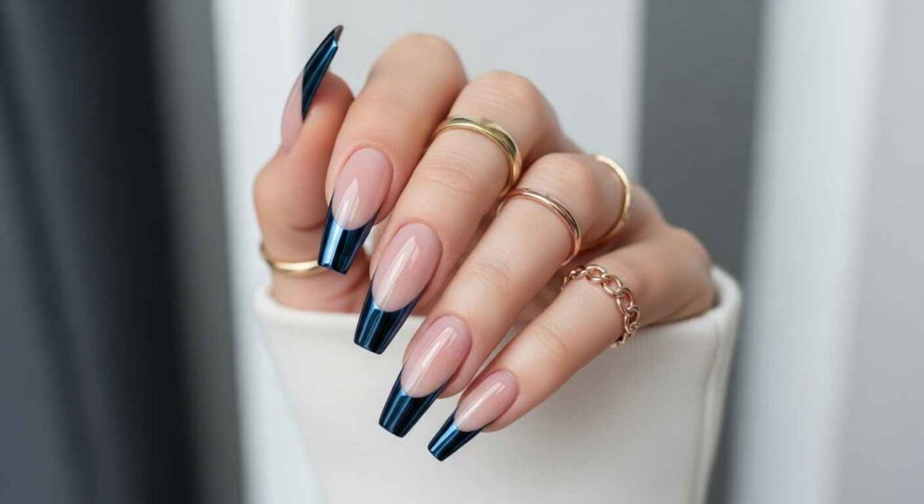 Nude almond nails with navy chrome French tips, shown on a hand wearing gold rings.