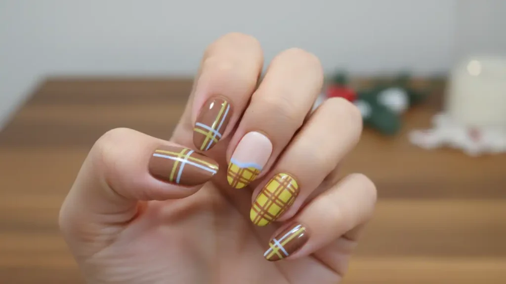 Muted yellow plaid nail design with brown tones and light blue stripes.